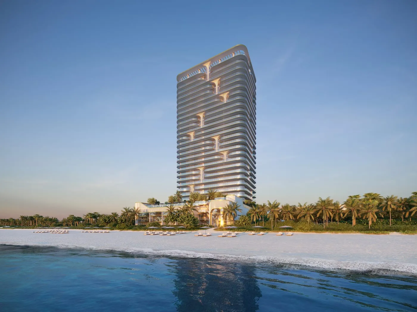 Modern high-rise building with curved balconies on a sandy beach lined with palm trees under a clear sky.